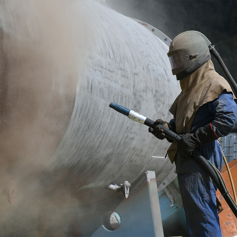 belis-sandstrahlen-1 Ein großes Rohr wird von einem Handwerker in Sicherheitskleidung gesandstrahlt